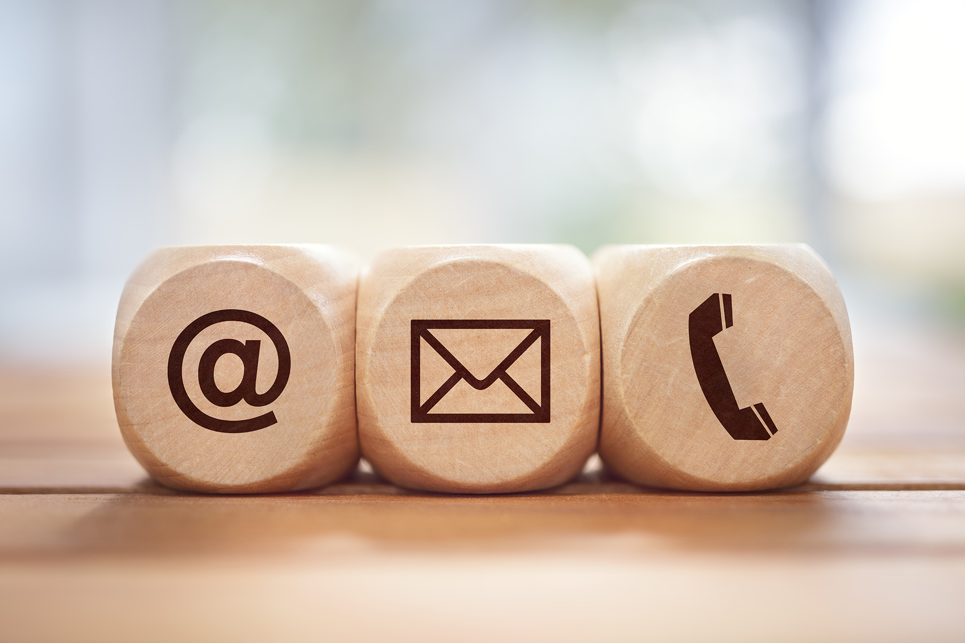 Picture of three wooden blocks with symbols: the first block shows ‘@’ for email, the second shows a mail icon for digital or paper mail, and the third shows a traditional phone receiver for phone calls.